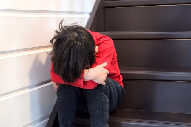 階段に座り込み顔を伏せる男の子