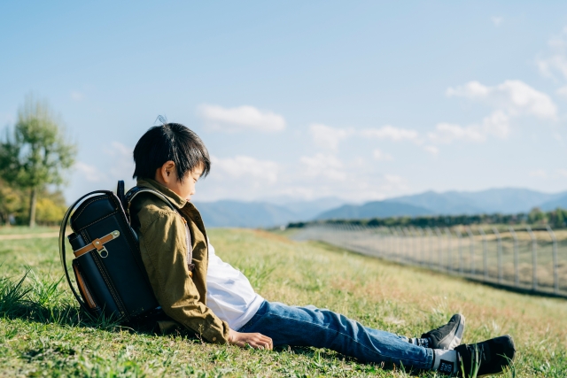 ランドセルを背負い芝生に一人で座っている男の子