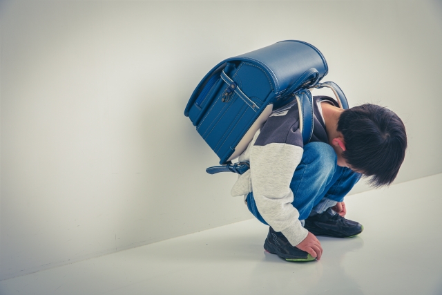ランドセルを背負いながら座り込む男の子