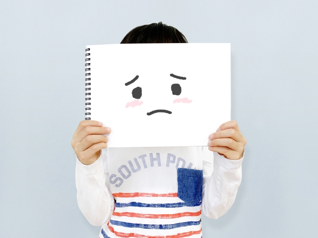 困った顔の絵を顔にあてる男の子